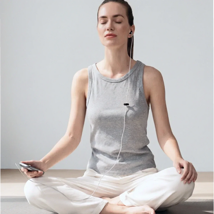 Woman sitting calmly while using a wired ear-based wellness device during a relaxation session