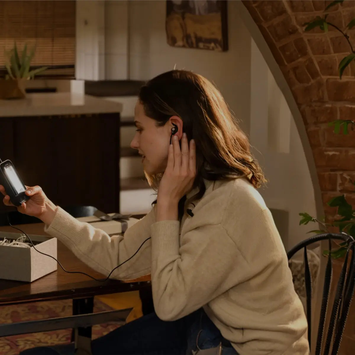 Woman wearing a ZenoWell ear-based device while holding the controller during a wellness session