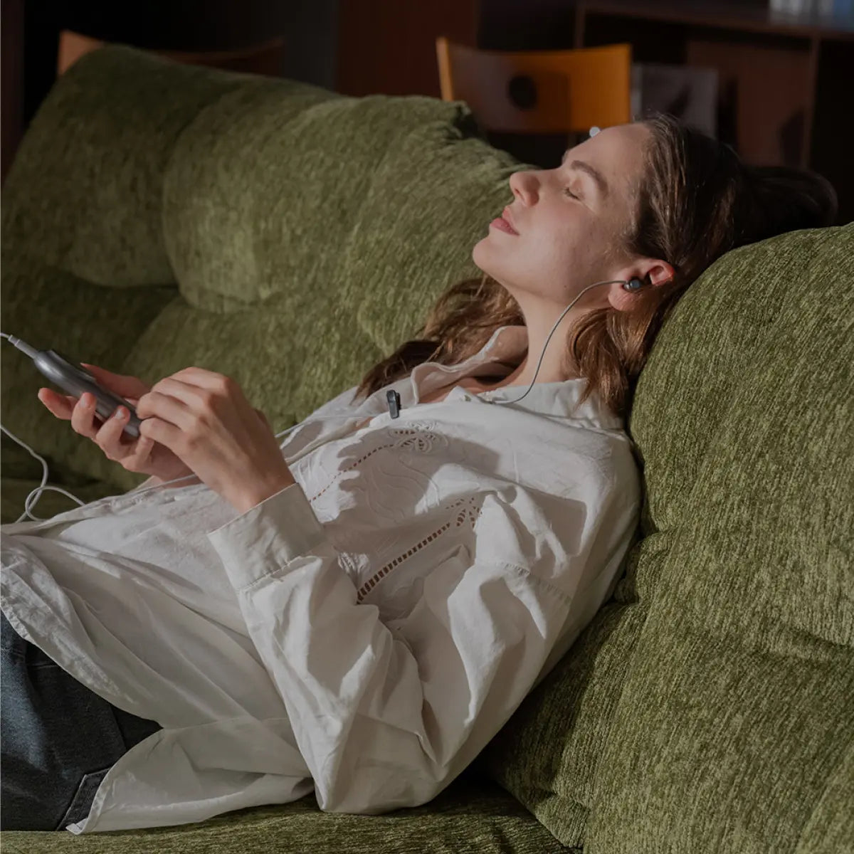 Woman relaxing on a sofa while using an ear-based wellness device during a quiet recovery routine