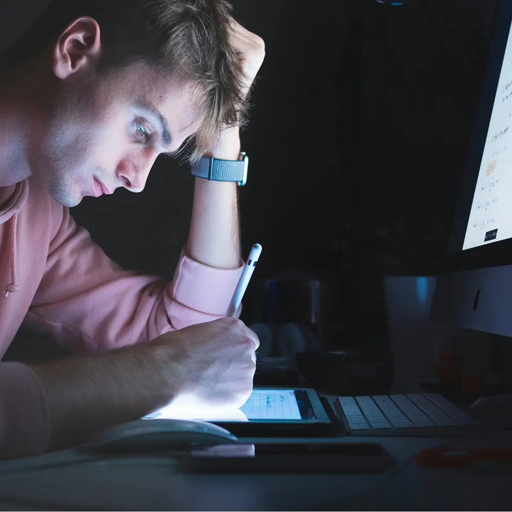 A person studying at night while struggling to maintain attention in front of a screen