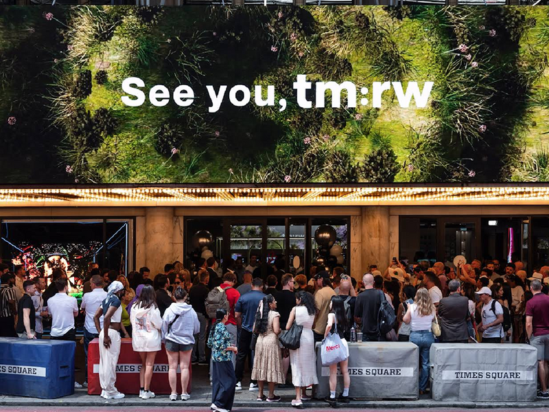Times Square crowd with "See you, tm:rw" billboard, representing wellness for tomorrow